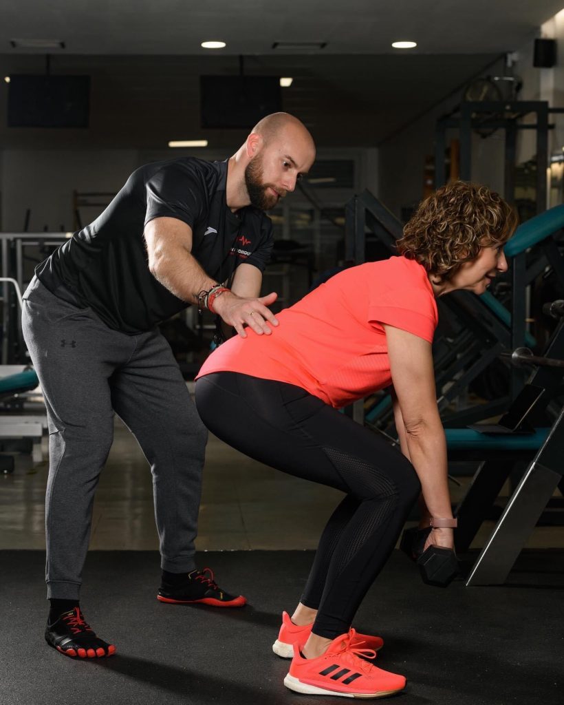 Iván entrenador corrigiendo postura en el ejercicio de una cliente que coge pesas